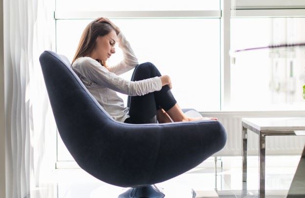 Woman sitting on a chair with her hand touching her head.